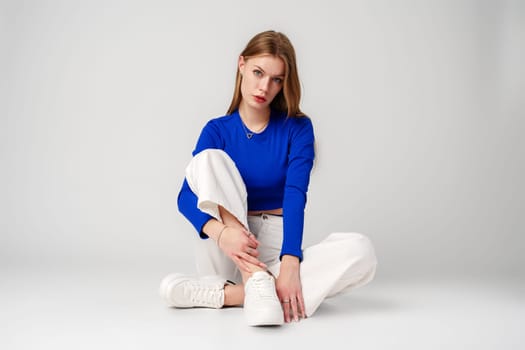 Young Woman model in Blue Top and White Pants posing on white background in studio