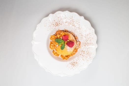 Fluffy pancakes with raspberries and mint leaves on a white plate against a clean white background. Close-up shot.