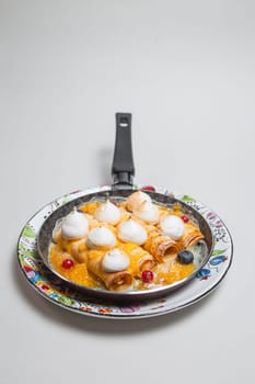 Pancakes with meringue and berries in a frying pan on a white background.