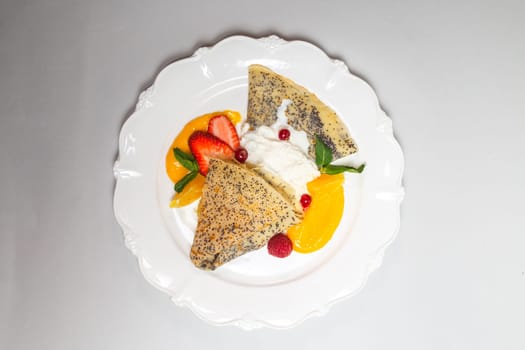 Delicious poppy seed pancakes with berries, orange slices and cream on a white background, a perfect breakfast treat.