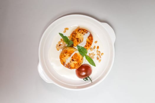 Two round fried cheese pancakes with sour cream and cherry tomatoes on a white plate on a white background. Isolated on a white background.