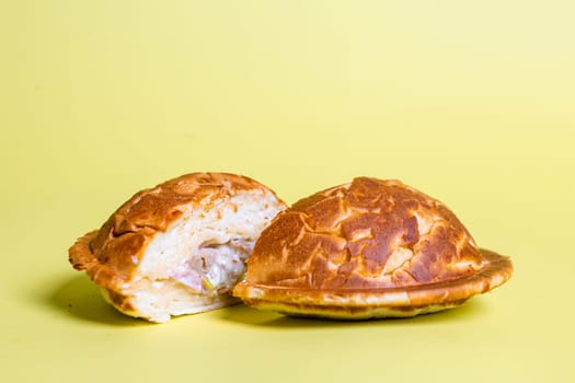 Half of burger with no top bread and a fried egg on top of the patty, isolated on a pastel yellow background.