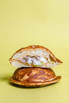 Half of burger with no top bread and a fried egg on top of the patty, isolated on a pastel yellow background.