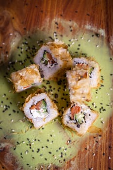 Delectable deep-fried sushi roll with fresh salmon, cucumber, on wooden plate with wasabi and sesame seeds, a Japanese delight.