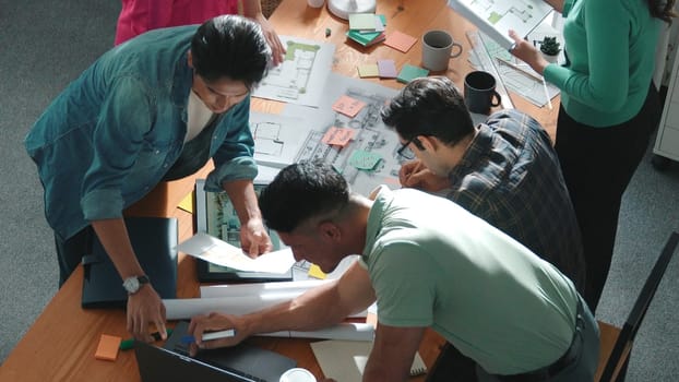 Top down of skilled business people holding tablet an looking at blueprint. Aerial view of architect engineer planning and design house design together while standing at table with laptop. Symposium.