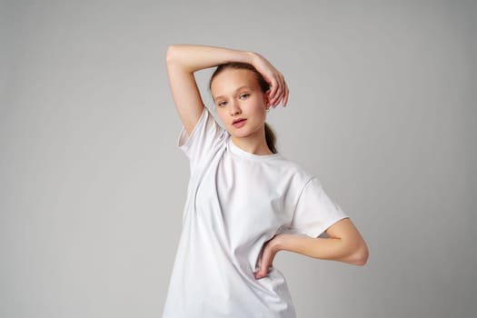 Beautiful young girl posing in white T-shirt and jeans on gray background in studio