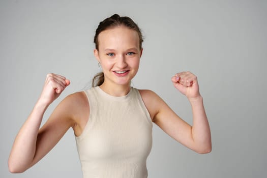 Young Woman in Casual Attire Smiling and Making a Fist Pump Gesture on a Plain Background close up