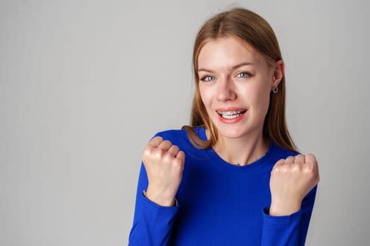 Smiling Young Woman in Blue Top Celebrating Success With Raised Fist in studio