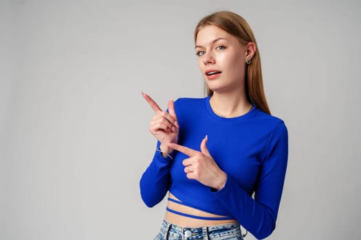 Woman in Blue Top Pointing With Hand Against Neutral Background in studio