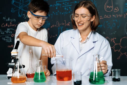 Teacher support schoolboy in laboratory. Schoolboy and teacher stand and experiment about science of chemistry in STEM class using liquid in glass container. Instructor mixing solution. Erudition.