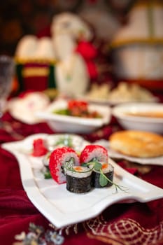 A variety of sushi rolls, along with other assorted dishes, are arranged on a table with a red tablecloth.