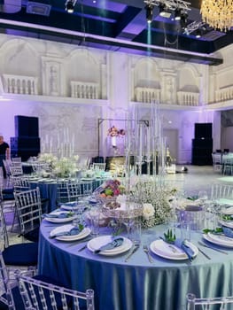 Elegant wedding reception hall with round tables, floral centerpieces, white and gold decor, and a spacious dance floor.