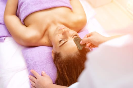 Relaxing massage. European woman getting quartz guache face massage in spa salon, side view.
