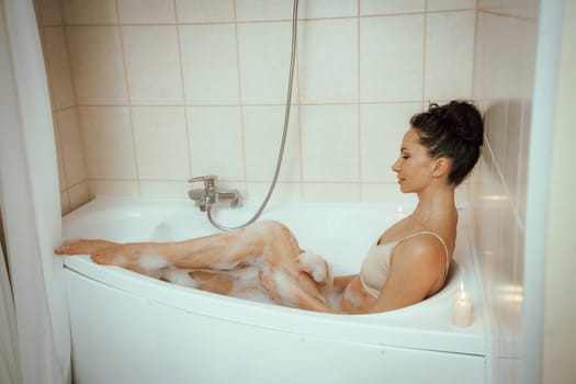 A woman is sitting in a bathtub with bubbles and candles. She is smiling and she is enjoying her bath