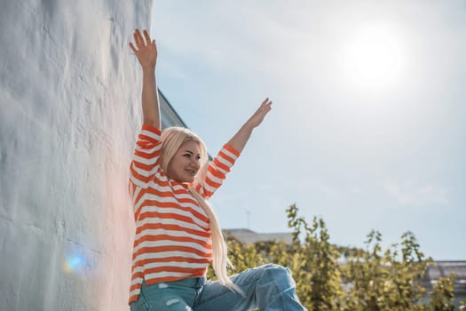 A woman is sitting on a railing with her arms raised in the air. The sun is shining brightly, creating a warm and inviting atmosphere