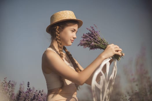 girl sitting field lavender and wearing a straw hat. She is smiling and holding a bouquet of flowers.