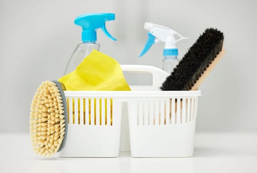 Table, brush or basket with supplies, spray bottle or chemical for bacteria, wellness or dirty mess in home. Grey background, cleaning service or ready for washing with product, liquid soap or gloves.