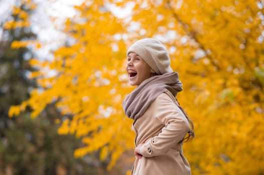Happy caucasian girl in a beige coat and beret walks in the park in autumn