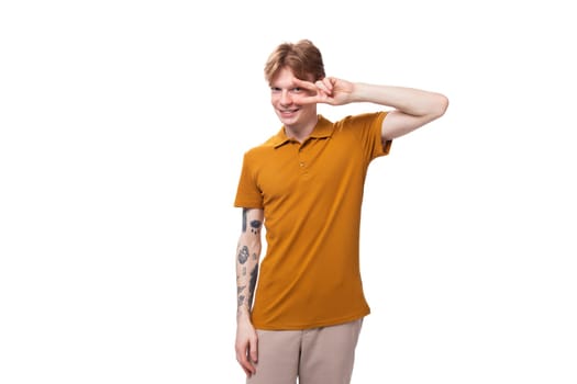 young red-haired guy dressed in an orange t-shirt smiles cutely on a white background.