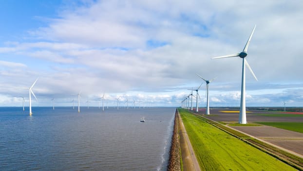 A row of majestic wind turbines stands elegantly next to a calm body of water under the clear Spring sky in the Netherlands. windmill turbines offshore and onshore in the Noordoostpolder Netherlands