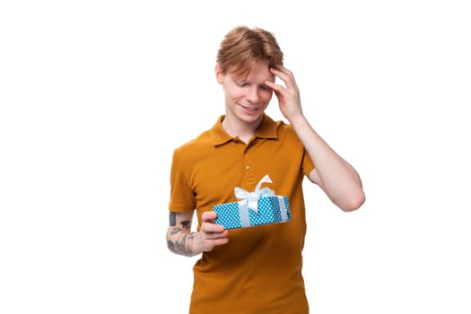 young man with red hair in an orange t-shirt holding a gift.