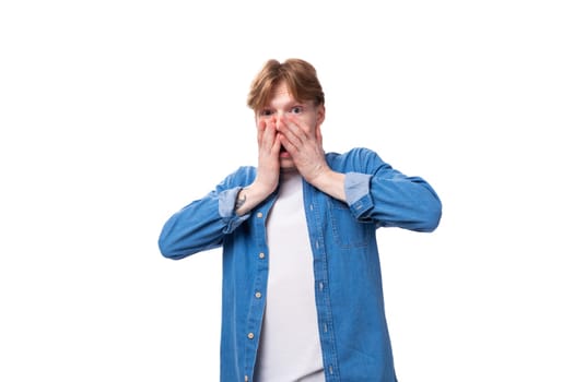 a young red-haired guy dressed in a blue shirt over a T-shirt looks at the camera in surprise.