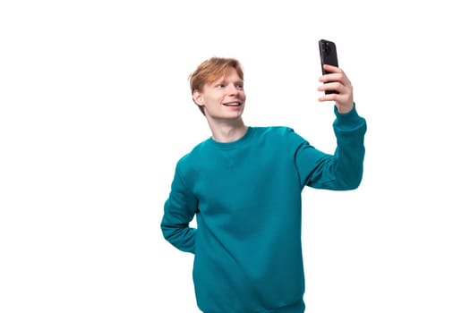 handsome red-haired young man in a blue sweater takes a photo on a smartphone.
