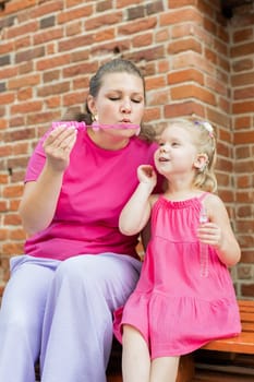 Deaf child with cochlear implant for hearing audio and aid for impairment having fun and laughs with mother outdoor in summer. Sound fitting device to help with communication listening and interaction.