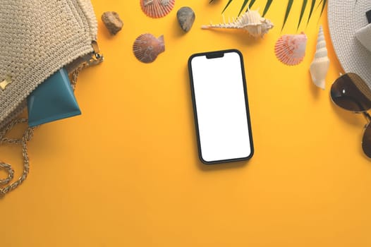 Smartphone with blank screen, sunglasses, straw hat and seashells on yellow background.