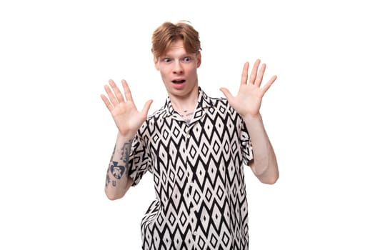 young european male student with red hair dressed in a patterned shirt is surprised.