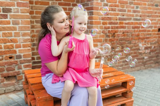 Deaf child with cochlear implant for hearing audio and aid for impairment having fun and laughs with mother outdoor in summer. Sound fitting device to help with communication listening and interaction.