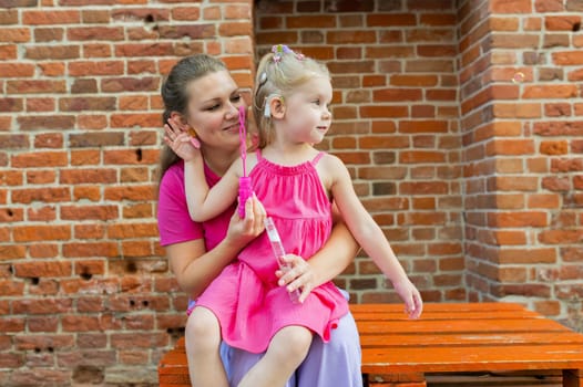 Deaf child with cochlear implant for hearing audio and aid for impairment having fun and laughs with mother outdoor in summer. Sound fitting device to help with communication listening and interaction.