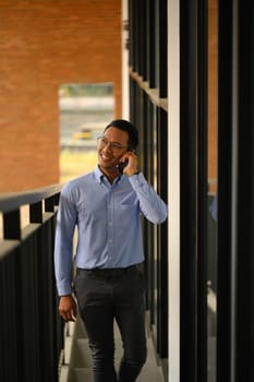 Positive businessman talking on mobile phone while walking up stairs the office building.