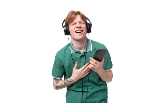 modern stylish energetic young red-haired guy in a green t-shirt listens to music in headphones.
