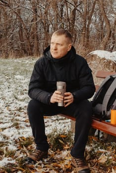 Winter Serenity: 40-Year-Old Man Enjoying Tea on Snow-Covered Bench in Rural Park. Immerse yourself in the tranquil beauty of winter as a 40-year-old man finds solace on a snowy bench in a rural park. Sipping hot tea from a thermos, he embraces the serene ambiance, surrounded by the peaceful, snow-covered nature. This captivating image captures the essence of winter leisure, offering a moment of seasonal joy and quiet contemplation amidst the breathtaking scenery.