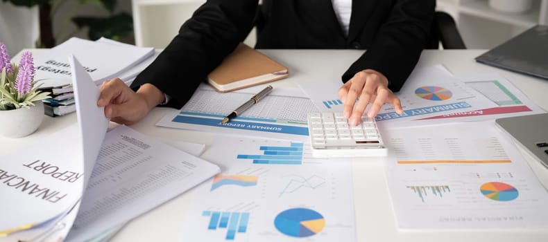 Asian female accountant Use a calculator to calculate business numbers on a white wooden table in the office..