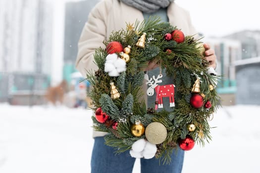 A person standing while holding a Christmas wreath adorned with a picture of a reindeer. The wreath is bright and festive, with a prominent image of a reindeer in the center.
