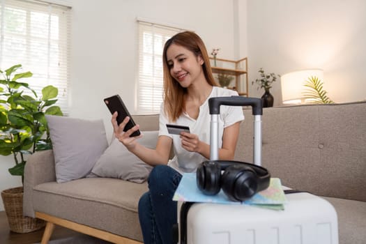 Asian woman using credit card booking flight tickets and hotel at home. Planning a trip and online booking, Summer vacation concept.