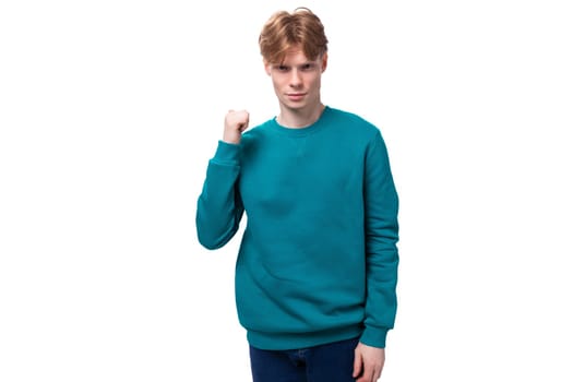 young confident man with red hair dressed in a blue sweater on a white background with copy space.