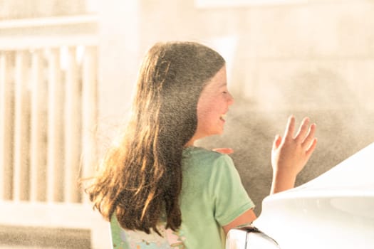 A joyful young girl gleefully gets soaked in refreshing water mist during a hot summer day.