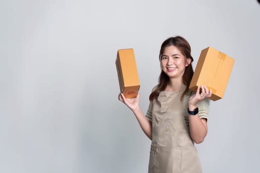 Young asian woman startup small business freelance holding parcel box and standing isolated on gray background, Online marketing packing box delivery concept.