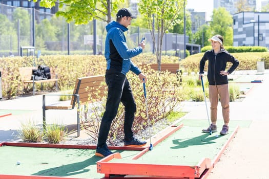 Sharing with golf experience. Cheerful young man teaching his daughter to play mini golf at the day time. Concept of friendly family. High quality photo