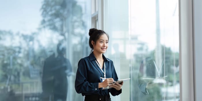 happy professional business woman working on tablet at work standing near window.