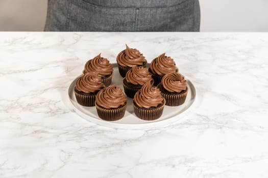 Freshly baked cupcakes have been masterfully infused with rich caramel and adorned with velvety chocolate frosting, all elegantly presented on a pristine white serving plate.