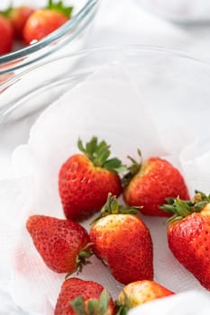 Bright red strawberries, interspersed with signs of mold, rest in a glass bowl lined with a paper towel on a white napkin, indicating improper storage techniques.