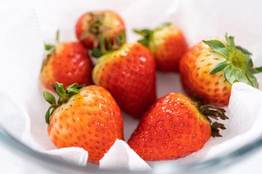 Freshly washed and dried strawberries are carefully arranged in a glass bowl lined with paper towel, ready for snacking or further use.