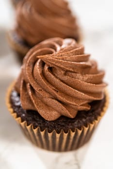 Delicate swirls of rich chocolate icing are meticulously piped onto each chocolate cupcake, creating an irresistible treat.