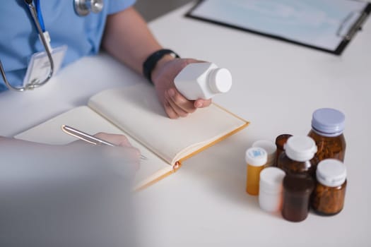 A doctor is writing in a notebook while holding a bottle of pills. Concept of professionalism and responsibility, as the doctor is taking notes on a patient's medication