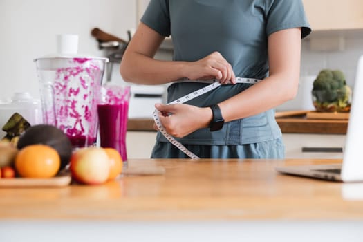 Close up a woman is standing in a kitchen, smiling and holding a measuring tape.