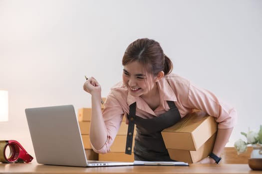 Startup SME small business entrepreneur SME of freelance Asian woman using a laptop with box Cheerful success Asian woman her hand lifts up online marketing packaging box.